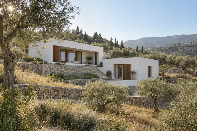 A white-plaster house embedded in olive terraces on a sunlit hillside.