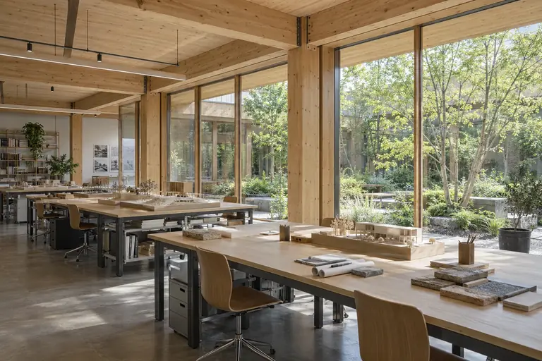 A bright mass-timber design workspace with architectural models and a garden beyond.